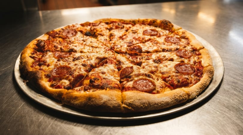 A whole pepperoni pizza, cut into slices, on a metal pizza pan.