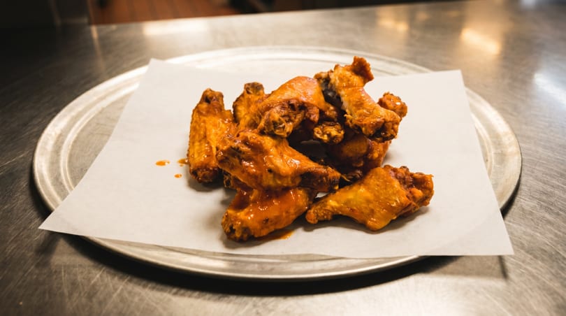 A pile of saucy, golden-brown chicken wings on parchment paper, served on a metal pizza pan.