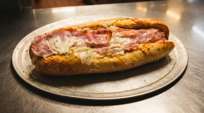 A toasted sub sandwich with ham and melted cheese on a metal tray.